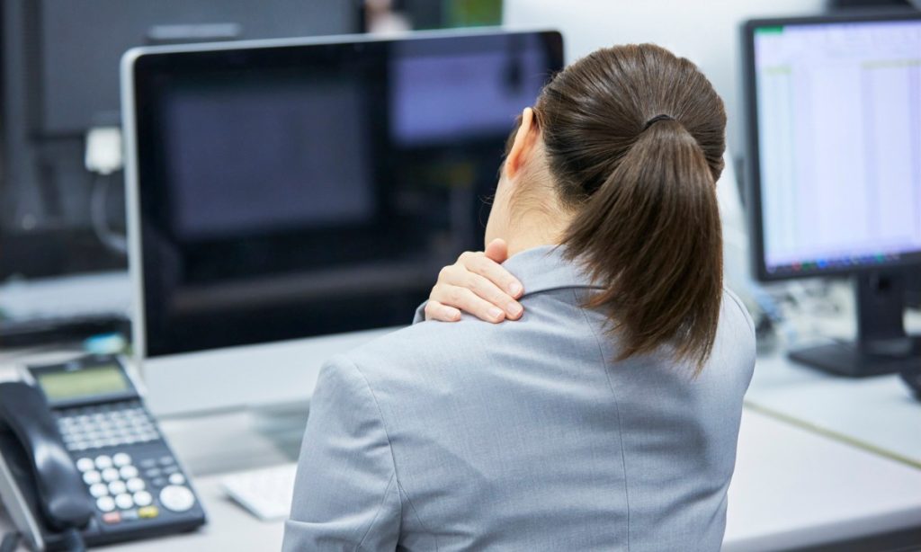 A woman sitting behind a desk with pain in her neck and upper back